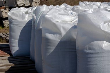 Dışarıdaki ahşap paletlerde beyaz ve büyük çantalar. Açık bir depoda depolanan mallar. Yan görüş. Güneşli bir bahar günü. Lojistik konular. Seçici odaklanma. İnsanlar olmadan.