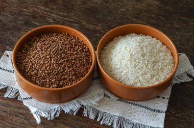 Pirinç ve karabuğday kaselerinde. Kuru tahıllı iki kase kil. Geleneksel yemek. Bir açıdan üstten bak. Çizik ve çatlaklarla dolu ahşap bir arka plan. Seçici odak.