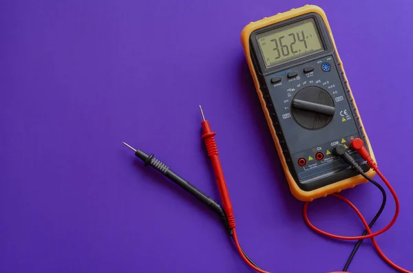Multimeter on a lilac background. Yellow Multimeter, A multimeter or a multitester is an electronic measuring instrument. A typical multimeter can measure voltage, current, and resistance. View from above