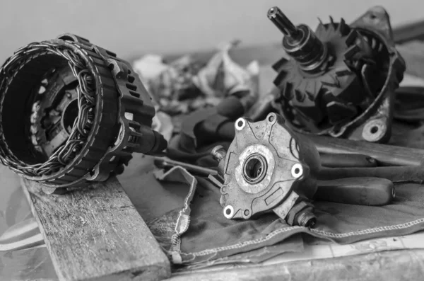 Details of a car generator on a workbench. Disassembled Used Automotive DC Generator. Repair used generator. Auto repair shop or service center. Selective focus. Black and white photo. Blurred background.