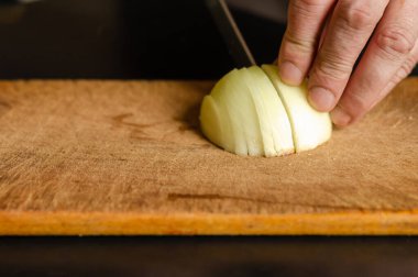 Kesme tahtasında soğan doğrama işlemi. Bir erkek eli, yarım bir soğanı bıçakla doğradı. Göz hizasında atış. Seçici odaklanma. Yakın plan..