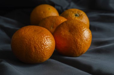 Siyah üzerine olgun mandalina. Beş kişilik bir mandalina grubu. Kabukta olgun narenciye meyveleri. Göz hizasında atış. Seçici odak.