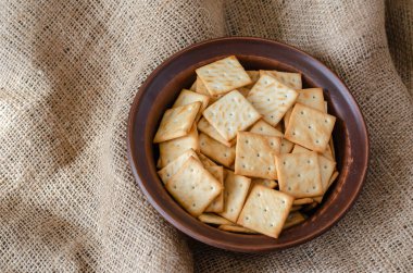 Çuval bezinde kil kasede tuzlu krakerler. Kare şekerlemelerle dolu bir kasenin en üst görüntüsü. Yakın plan. seçici odak.