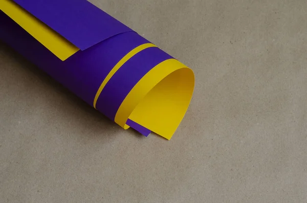 Roll of colored paper on a beige background. Blue and yellow sheet are twisted into a roll. Abstract background. Selective focus. Close-up.