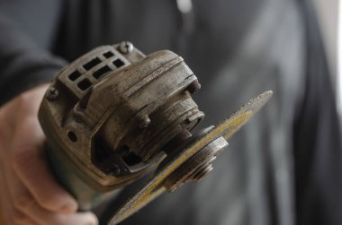 Adamın biri kameraya açı öğütücü uzatıyor. Elinde küçük bir elektrikli alet var. Üretimde iş güvenliği. Seçici odaklanma. Bulanık arkaplan.