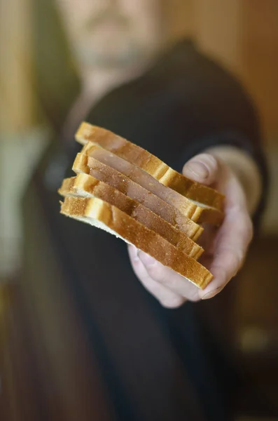 A man shares food. A male hand holds out pieces of bread into the camera. Helping the poor and needy. Selective focus. Blurred background.