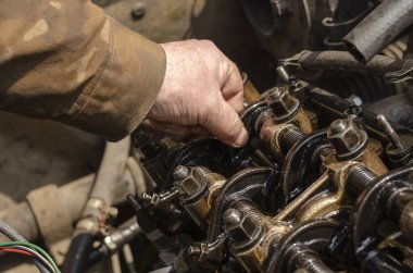 Benzin motorunun emme vanalarının termal izinlerini kontrol ediyorum. Yaşlı bir tamirci kontrol ediyor. Kapakçık kapağı olmadan karbüratör motorunun detaylı görüntüsü. Yan görüş. Seçici odak.
