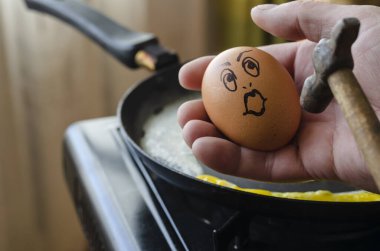 Elinde bir çekiç, elinde sürpriz tavuk yumurtası. Çiğ tavuk yumurtası, omletle birlikte bir tavanın üzerine süpriz bir tava. Asla pes etme. Açılı yan görüş. Yakın plan. Seçici odak.