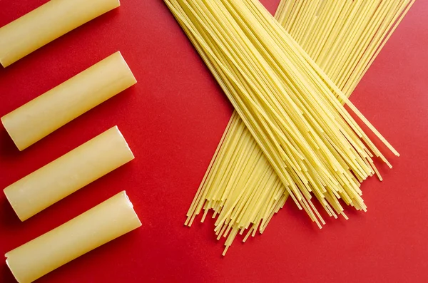 Cannelloni and spaghetti on a red background. Dry cannelloni tubules and spaghetti straws. Unprepared pasta. View from above. Selective focus.