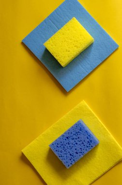 Sarı arka planda mutfak süngeri ve temizlik peçeteleri. Bir çift gözenekli sünger ve peçete. Ev rutini ve ticari temizlik şirketi. Seçici odak.