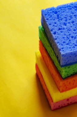 Mutfak gözenekli süngerler. Sarı arka planda çok renkli mutfak süngeri yığını. Temizlik için yeni parlak aksesuarlar. Ticari temizlik şirketi. Seçici odak.