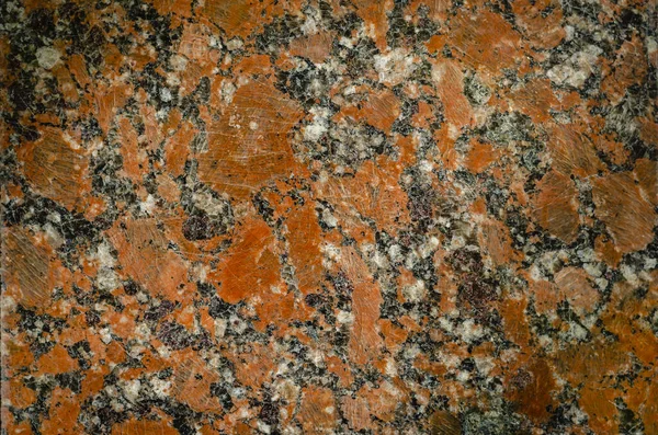 Red granite background. The texture of the old granite. Red polished granite with scratches and cracks. The texture of natural stone. Close-up.
