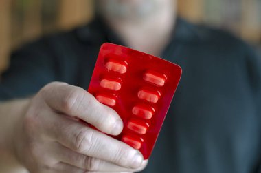 Haplarla su toplayan bir adam. Kameradaki yetişkin bir erkeğin eli hapları tutuyor. Erkeklerde cinsel sağlık kavramı. Ön plana odaklan. Bulanık arkaplan.