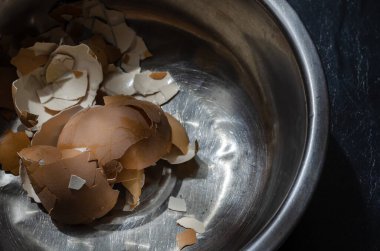 Metal bir kasede yumurta kabukları. Haşlanmış tavuk yumurtalarının kahverengi kabuğu paslanmaz çelik bir kasede. Yemek pişirme süreci. Yiyecek atıkları. Bir açıdan üstten bak. Yakın plan. Seçici odak.
