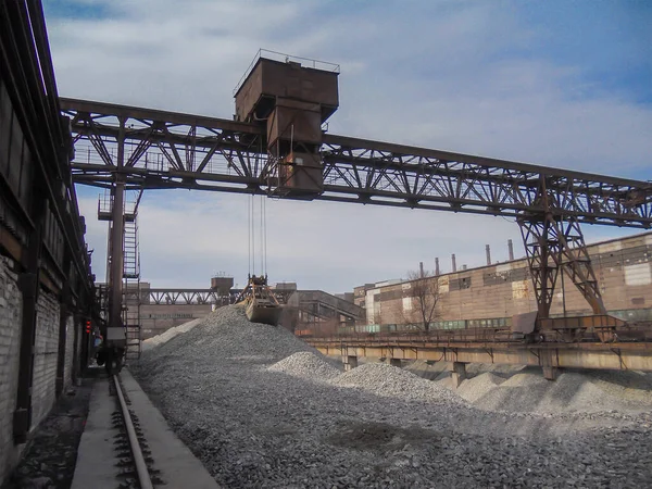 The process of loading crushed stone with a gantry crane. A rusty grab crane will perform cargo operations in the rubble warehouse. Large warehouse in the open. Industrial background. Selective focus.