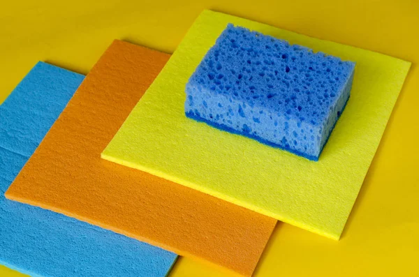 黄色の背景にクリーニングとスポンジのためのキッチンナプキン 3色の多色の食器用ナプキンと青い多孔質キッチンスポンジ クリーニングのための製品 選択的焦点 — ストック写真