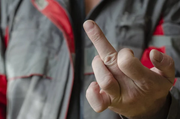 A man shows the camera a middle finger gesture up. Mechanic in red and gray working uniform with indecent gesture. Conflict in the workplace. Disobedience. Close-up. Selective focus.