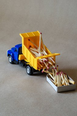 Mavi taksisi olan sarı bir damperli kamyon kibrit taşır. Tahta kibritlerle dolu bir oyuncak kamyon. Yaratıcı endüstriyel geçmiş. Kütük ve lojistik. Seçici odak.