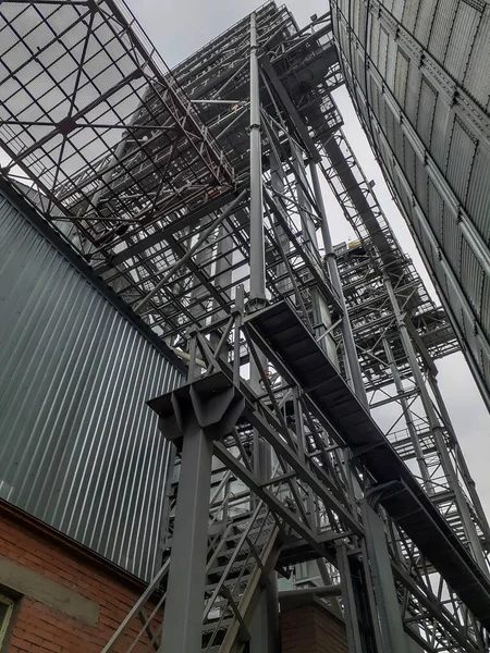 Metal structures of a modern grain elevator. Beams and trusses next to a cylindrical silo for storing grain. Industry and agriculture. Shooting from the bottom up. Selective focus.
