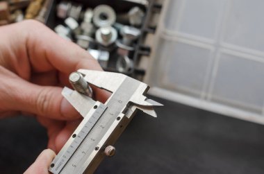 Kalibreye sahip bir erkek eli bir cıvatanın çapını ölçer. Doğru metal bağlayıcıyı seçiyorum. Elle ölçüm aletleri kullanılıyor. Ön plana odaklan. Yakın plan..