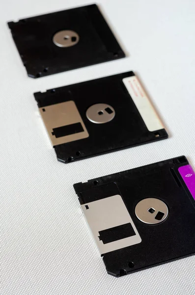Three floppy disks on a white textured background. Floppy disks with a capacity of 1.44 MB. 3.5 inch magnetic floppy disks. Obsolete digital data storage media. Close-up. Selective focus.