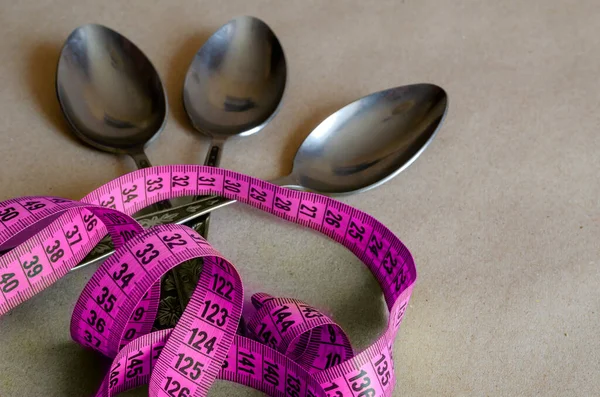 Tailor meter and three tablespoons. Measuring tape on top of three metal soup spoons. The concept of overeating during psychological problems. . Selective focus. — Stock Image Tailor Meter Three Tablespoons Measuring Tape Top Three Metal Soup Stock Picture