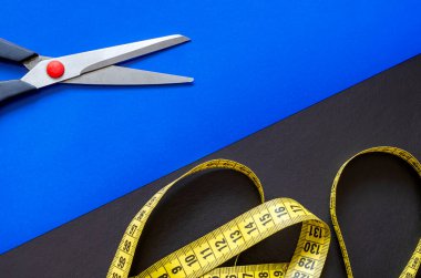 İki renkli arka planda makas ve mezura. Siyah ve mavi arka planda sarı terzi metresi ve makas. Çoklu görev geçmişi. Mesaj için yer. Yukarıdan görüntüle.