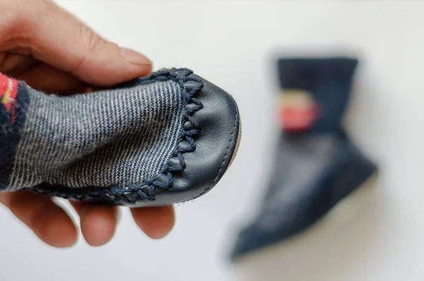 Soft shoes for babies in the hand. The male palm holds a small blue shoe. A pair of blue shoes with soft leather soles. Top view at an angle. Selective focus. Blurred background.
