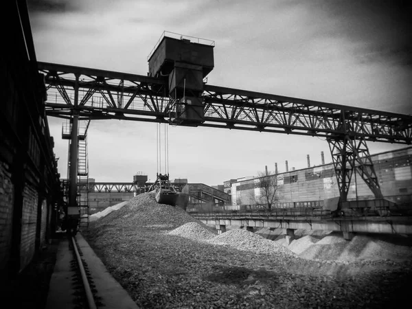 The process of loading crushed stone with a gantry crane. A rusty grab crane will perform cargo operations in the rubble warehouse. Large warehouse in the open. Industrial background. Selective focus.