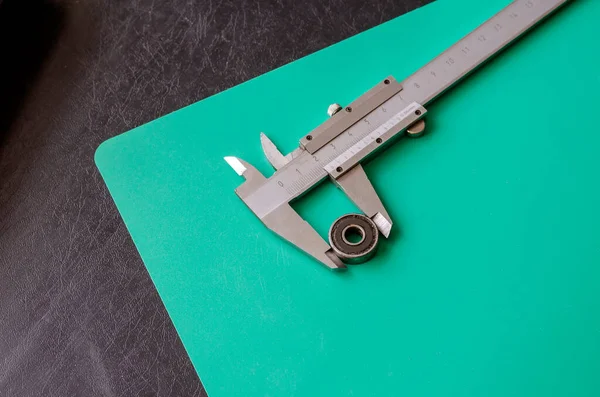 Ball bearing and vernier caliper on a black and turquoise background. Metal vernier caliper with decimal measurement system. Calculation of the dimensions of the old bearing for replacement.