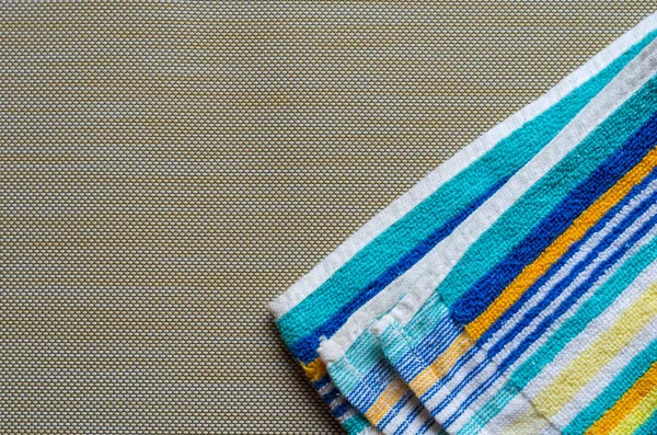 Multi-colored striped beach towel close-up. Colorful rainbow colored towel on a light brown textured background. Positive colors. Abstract background. View from above.