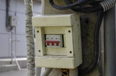 Dışarıdaki beton bir sütunun üzerinde eski bir üç direkli elektrik düğmesi. Açık hava aydınlatma düğmesi tozlu, çamurlu ve örümcek ağlı. Elektrik emniyeti. Seçici odak.