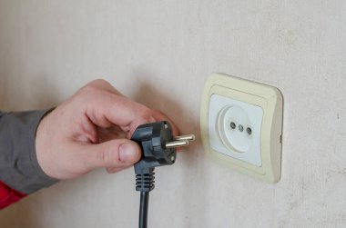 Elektrik prizinin 25. bölümünün tamiri. İş kıyafetleri içindeki bir adam duvar prizinden elektrik fişini çeker. Profesyonel bir elektrikçinin ticari hizmetleri. Seçici odak.