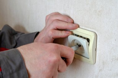 Elektrik prizinin 45. bölümünün tamiri. İş elbiseli erkek eller elektrik prizinin dekoratif kaplamasını kaldırır. Profesyonel bir elektrikçinin ticari hizmetleri. Seçici odak.