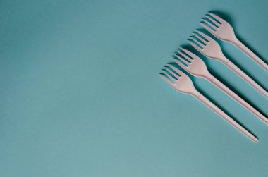 Açık turkuaz arka planda dört plastik çatal. Çizgi halinde yeni beyaz çatallar. Minimalist çoklu görev geçmişi. Yukarıdan görüntüle.