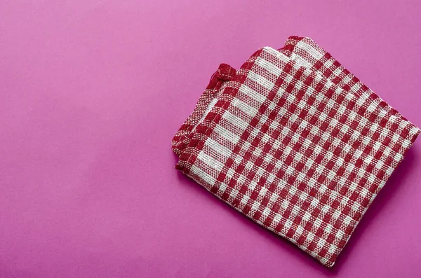 Light pink background with a white and red checkered towel. Kitchen linen towel folded on a color table. Minimalistic multitask background. View from above.