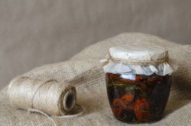 Çuval bezinde güneşte kurutulmuş domatesli kapalı cam kavanoz. Zeytinyağlı, sarımsak ve baharatlı domates konservesi. Ev yapımı konserve yiyecekler. Yakın plan..