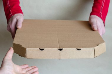 Kırmızı tişörtlü bir adam bir kutu pizzayı bir kadının eline geçiriyor. Alıcıların siparişlerini müşteriye aktarma işlemleri. Ürünlerin teslimatı. Alıcı tarafından çekiliyor..