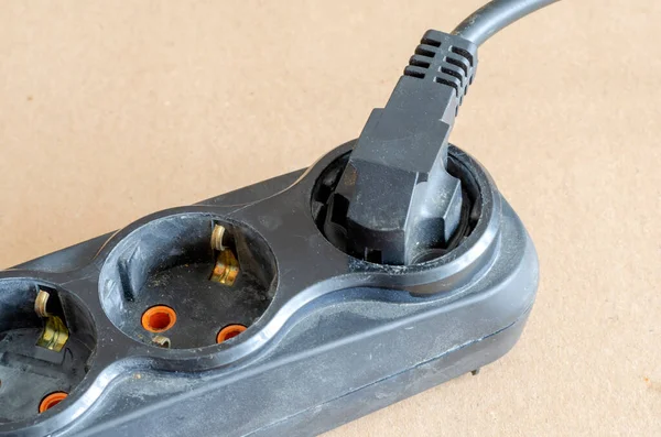 Used electric extension cord on a beige background. Black developer with a plug in the plug. Electrical Safety Rules. Close-up. Selective focus.