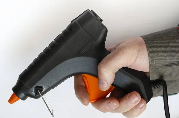 Hand holds an electric glue gun. Man in gray protective clothing. Using a hand tool. Close-up. Selective focus.