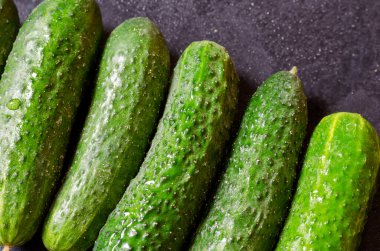 Bahçeden yeni toplanmış sebzelerin yakın çekimi. Karanlık bir masada taze kokulu salatalıklar. Yeni mahsul mevsimi. Kendi kendini yetiştirmiş sebzeler. Bir açıdan üstten bak. Seçici odak.