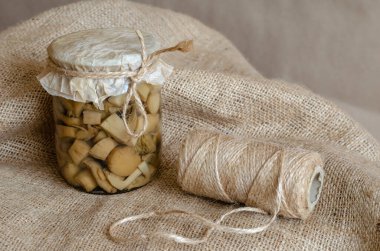 Çuval bezinde konserve mantarlı cam kavanoz. Mantarlı cam kase ve sicim yakın plan. Uzun vadeli depolama ürünleri.