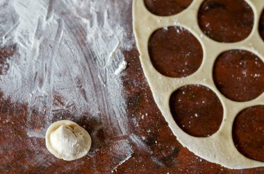 İnce hamurlu mutfak masası, un ve tek bir çiğ hamur köftesi. Et ile ev yapımı etli börek pişirmek. Küçük bir aile şirketi. Yukarıdan bak. Seçici odak.