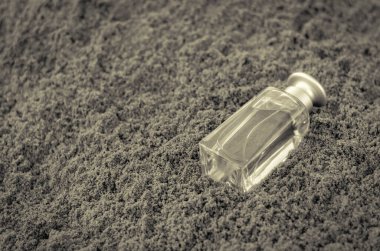 Kumda parfüm şişesi. El değmemiş bir sabah kumsalında dikdörtgen cam şişe. Parfüm endüstrisi. Bir açıdan üstten bak. Seçici odaklanma. Tek Renkli