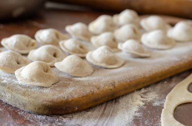 Kesme tahtasının üzerinde et ile pişirilmemiş hamur tatlısı. Mutfak masasına un serpiştirilmiş taze hamur tatlısı. Küçük bir aile şirketi. Göz hizasında atış. Seçici odak.