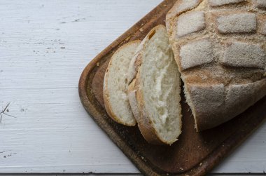 Beyaz ahşap arka planda taze pişmiş ev yapımı ekmek. Kesme tahtasında iki dilimlenmiş dilim ve bir somun kokulu sıcak ekmek. Küçük bir aile şirketi. Boşluğu kopyala.