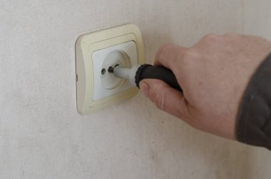 İş kıyafetleri içindeki el adamı tornavida bükerek duvardaki prizden vida monte ediyor. Profesyonel bir elektrikçinin ticari hizmetleri. Seçici odak