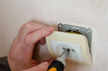 İş elbiseli erkek eller elektrik prizinin dekoratif kaplamasını kaldırır. Profesyonel bir elektrikçinin ticari hizmetleri. Seçici odak.