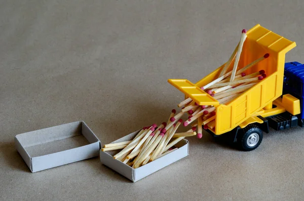 A yellow toy dump truck spills matches. A toy truck unloads a full body of wooden matches. Creative industrial background. Logistic topics. Selective focus.