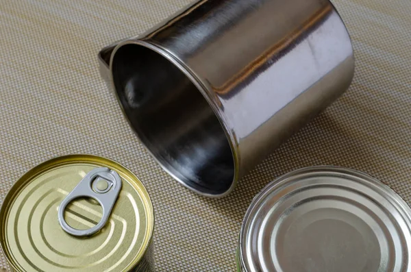 Two metal mugs and a can of canned food on a textured background. Stainless steel mugs next to canned food. Crockery and food for hiking, fishing, hunting. View from above.